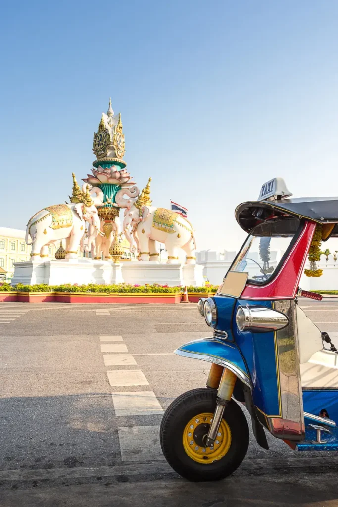 Thai tuk-tuk with a landmark sculpture in the background