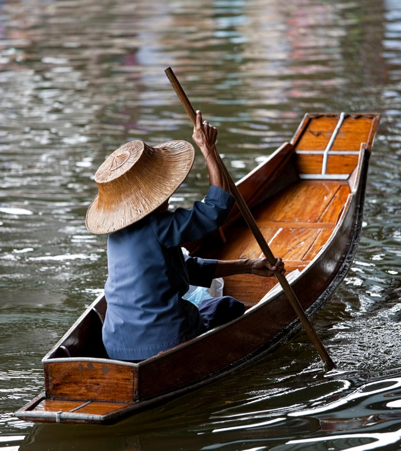 a man rows his traditional boat at damnoen saduak floating market in thailand.