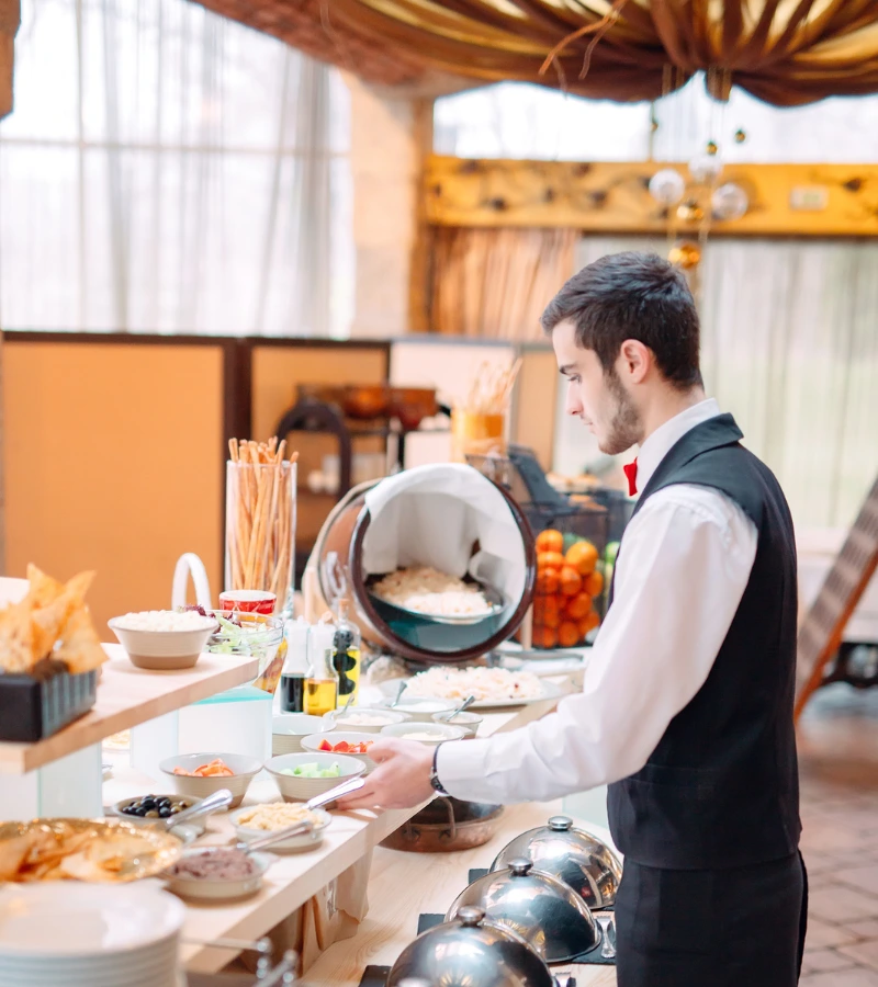 waiter preparing breakfast buffet at hotel restaurant